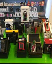 Vape-Shop-Auslage mit verschiedenen E-Zigaretten-Modellen und Zubehör auf einem grünen Tisch.