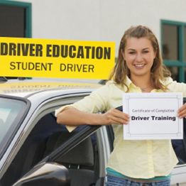 Woman holding driver training certificate next to car with "Student Driver" sign.