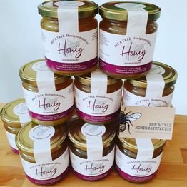 Ein Stapel von neun Honiggläsern der Marke "BEE TREE", auf einem Holztisch angeordnet.