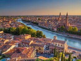 Vista aerea di Verona al tramonto, con fiume Adige e storici edifici in mattone rosso.