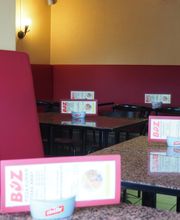 Leeres Café mit roten Sitzbänken, vier Tischen und Speisekarten auf dunklen Tischplatten.