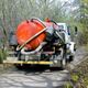 Truck with red tank and hoses driving on a forest road.
