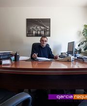 Hombre en oficina, sentado en escritorio con papeles, ordenador y plantas.