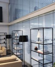 Salotto moderno con divani beige, piante, scaffali e una grande finestra con tende.