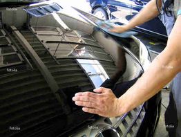 Person poliert die Motorhaube eines glänzenden schwarzen Autos in der Werkstatt.