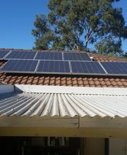 Paneles solares en un techo de tejas bajo un cielo azul, rodeados de árboles.
