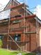 Rotes Backsteinhaus mit Gerüst, vorbereitet für Außenarbeiten, blauer Himmel im Hintergrund.