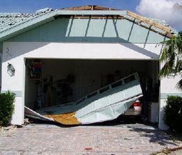 Damaged garage with a collapsed door, exposing a car inside; roof partly missing.