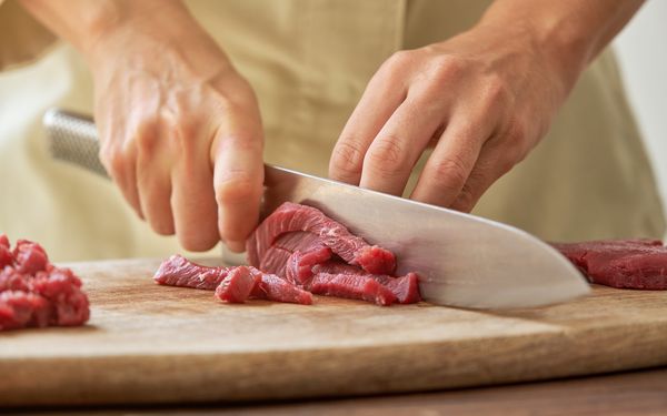 Fleisch wir auf Holzbrett mit einem großen und scharfen Messer in dünne Scheiben geschnitten