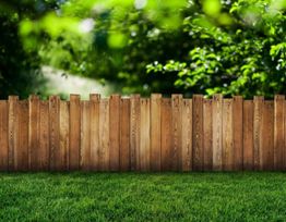 Wooden fence with a lush green lawn and leafy trees in the background.