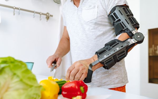 Mann mit Orthese steht in seiner Küche und schneidet eine gelbe Paprika klein.