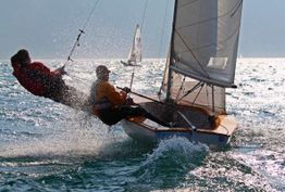 Segelboot mit zwei Personen, die sich gegen den Wind lehnen, während es über das Wasser gleitet.