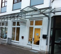 Außenansicht eines weißen Gebäudes mit vielen Fenstern und einem Schild mit der Aufschrift „SÄNDIG“.