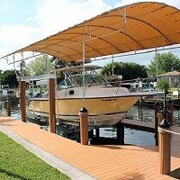 Boat under a canopy on a dock by the water with trees and houses in the background.