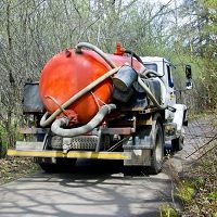 Septic truck with a red tank parked on a narrow forest road.