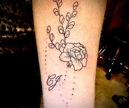 Een tatoeage met bloemen, takjes, initialen "C J" en een klein hartje op een onderarm.