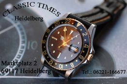 Klassische Armbanduhr mit schwarzem Zifferblatt und goldenen Details, Text zu Standort in Heidelberg.