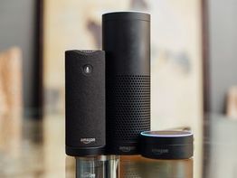 Three Amazon Alexa devices on a reflective surface.