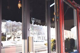 Glass door with "Elevate" sign, reflective street view, and decorative hanging ornaments.