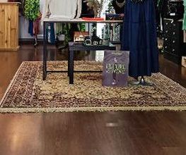 Tienda de ropa con maniquíes, alfombra y prendas exhibidas. Ambiente acogedor y colorido.