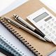 A calculator, pens, and notebooks stacked neatly on a white surface.