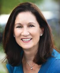 Smiling woman with shoulder-length dark hair wearing a blue top outdoors.