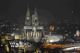 Kölner Dom bei Nacht, von Lichtern der Stadt und beleuchteten Gebäuden umgeben.