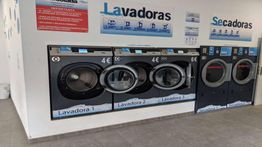 Lavadoras y secadoras en una lavandería automática con precios en euros.