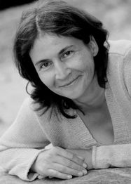 Frau lächelt in die Kamera, liegt entspannt auf einem Stein, trägt Pullover, schwarz-weiß Bild.