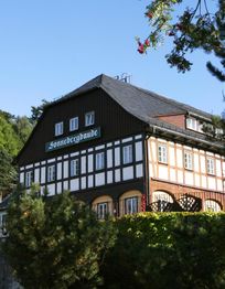 Fachwerkhaus im Grünen mit Schild "Sonnebergbaude", blauer Himmel, Zweige mit roten Beeren.