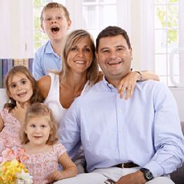 A happy family of five posing together in a bright living room, with smiles and relaxed expressions.