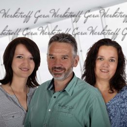 Eine Frau, ein Mann und eine andere Frau lächeln vor einem Hintergrund mit Schriftzug.