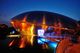 Futuristisches Gebäude bei Nacht, beleuchtet in Blau und Orange, mit Spiegelung im Wasser.