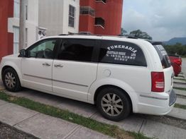 Minivan blanca de funeraria estacionada frente a un edificio rojo y blanco.