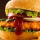 Hamburger con lattuga e ketchup, contornato da patatine fritte. Sfondo scuro sfumato.