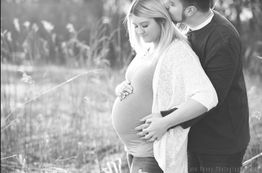 Pregnant woman embraced by partner in a peaceful field setting.