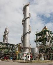 Refinaria industrial com estruturas metálicas e tanques sob céu nublado.