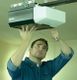 Man fixing a garage door opener mounted on the ceiling, wearing a denim shirt.