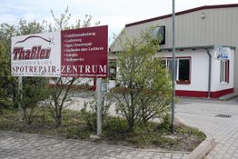 Gebäude mit Werbeschild: "Thaler Karosserie & Lack Spotrepair-Zentrum", umgeben von Büschen.