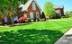 Manicured lawn in front of brick houses with trees and clear blue sky.