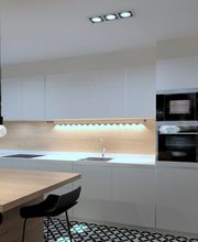 Cocina moderna con muebles blancos, mesa de madera, lámparas colgantes y electrodomésticos.