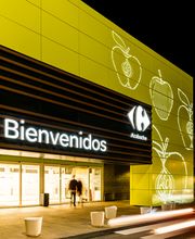 Fachada iluminada de un supermercado con el letrero "Bienvenidos" en letras brillantes.