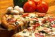 Pizza mit Peperoni, Oliven, Paprika und Pilzen, umgeben von Tomaten und Pilzen auf Holztisch.