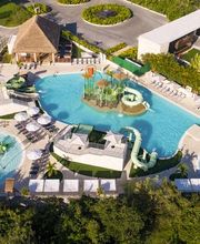 Vista aérea de un resort con múltiples piscinas y áreas de descanso cerca de un edificio moderno.