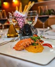 Langosta gourmet servida en un restaurante elegante, con copas de vino al fondo.