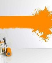 Farbeimer und Rolle vor einer Wand mit orangefarbenem Farbfleck und Streifen.