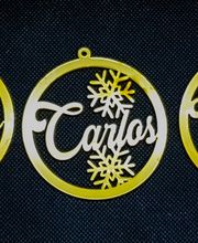 Adornos navideños dorados con nombres Jesús, Carlos y Wilfredo y copos de nieve.