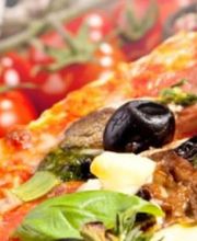 Pizza mit Oliven, Basilikum und Kirschtomaten im Hintergrund.