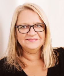 Eine lächelnde Frau mit blonden Haaren und Brille schaut in die Kamera.