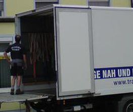 Umzugs-LKW vor einem Gebäude, Möbel werden mit einer Außenleiter in obere Etagen transportiert.